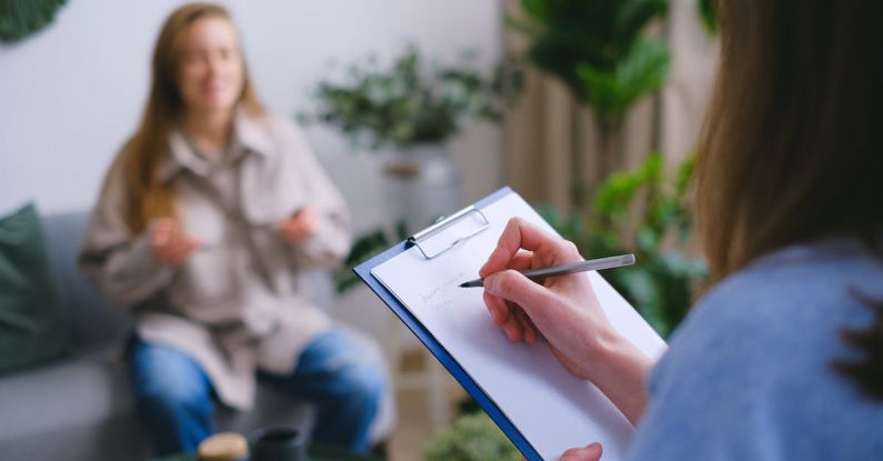 Dilemmas - Unrecognizable professional female psychologist writing on clipboard while sitting against client on blurred background during psychotherapy session in light office