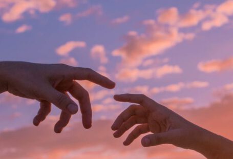 Green Bonds - Crop anonymous people pulling hands to each other against bright sunset sky with clouds