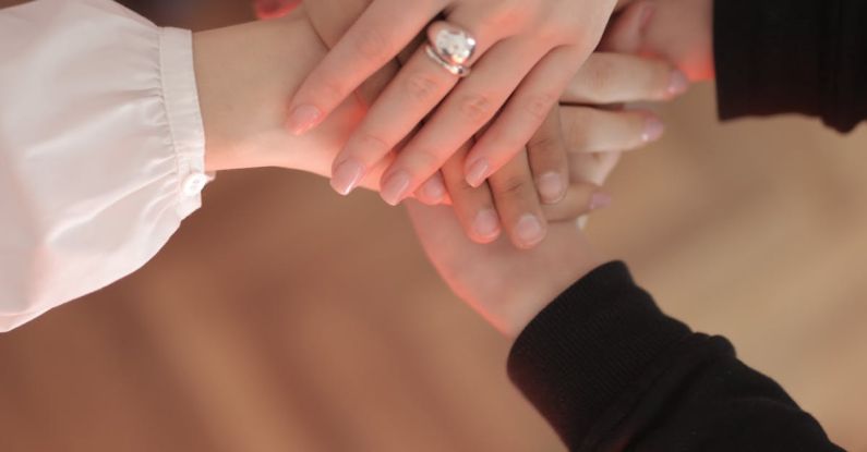 Communicating Partnerships - Top view of faceless friends in different clothes stacking hands together while standing on wooden floor indoor on sunny day