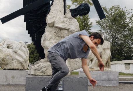 Attract Talent - Young flexible man wearing casual outfit performing breakdance against modern monument Way of cross located in park of Moscow city Russian Federation